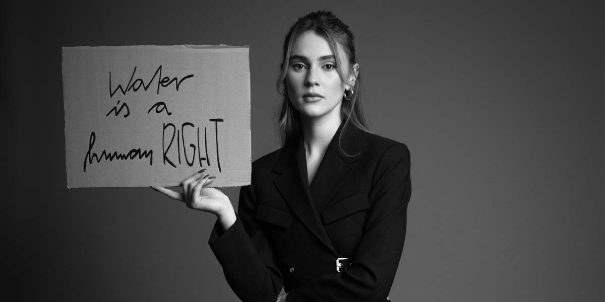 viva-con-agua-campaign-stefanie-giesinger-black-and-white-sitting-chair-holding-sign-water-is-a-human-right