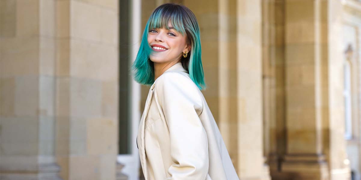 vanessa-interview-teal-hair-smiling-long-bob-beige-suit-outdoor-building-posing-from-the-side